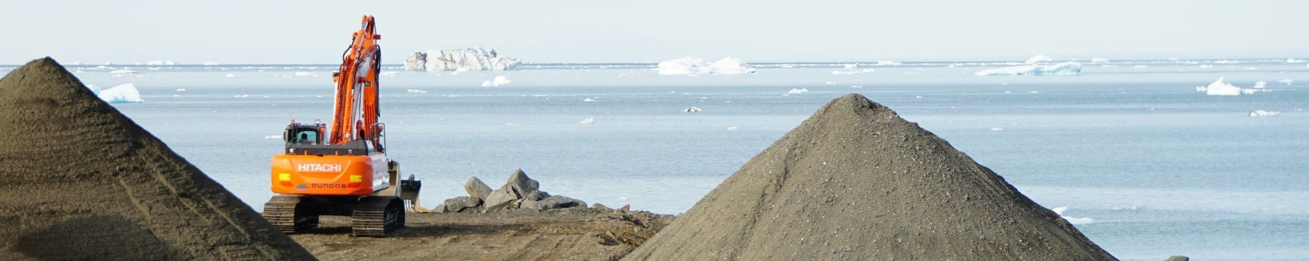 Image of shale piles and machinery with grey sea in background.