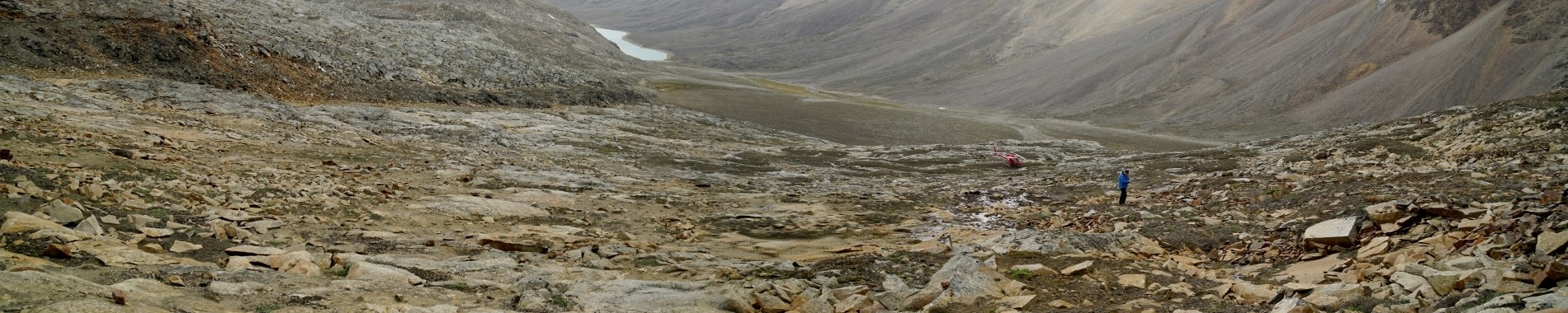 Image of a glacial valley with red helicopter landed at distance